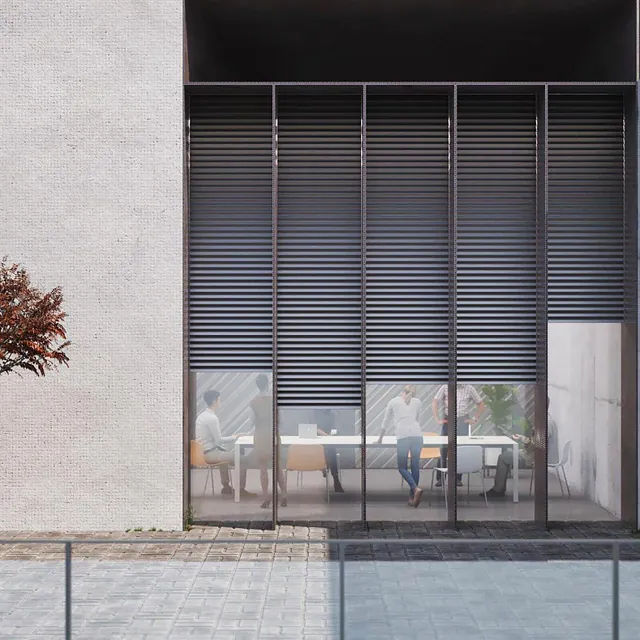 Moderne bygning med store vinduer hvor personer sitter rundt et bord, sett utenfra.